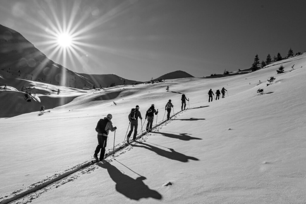 Black and white photo of a group skiing in mountainous terrain under bright winter sun.