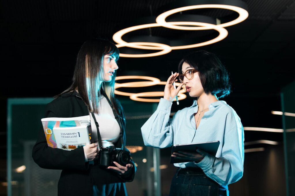 Two women in a modern office discussing with digital devices, highlighting contemporary teamwork.