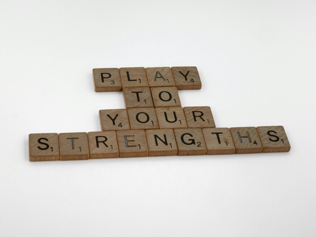 Motivational message 'Play to Your Strengths' made from wooden Scrabble tiles on a white background.