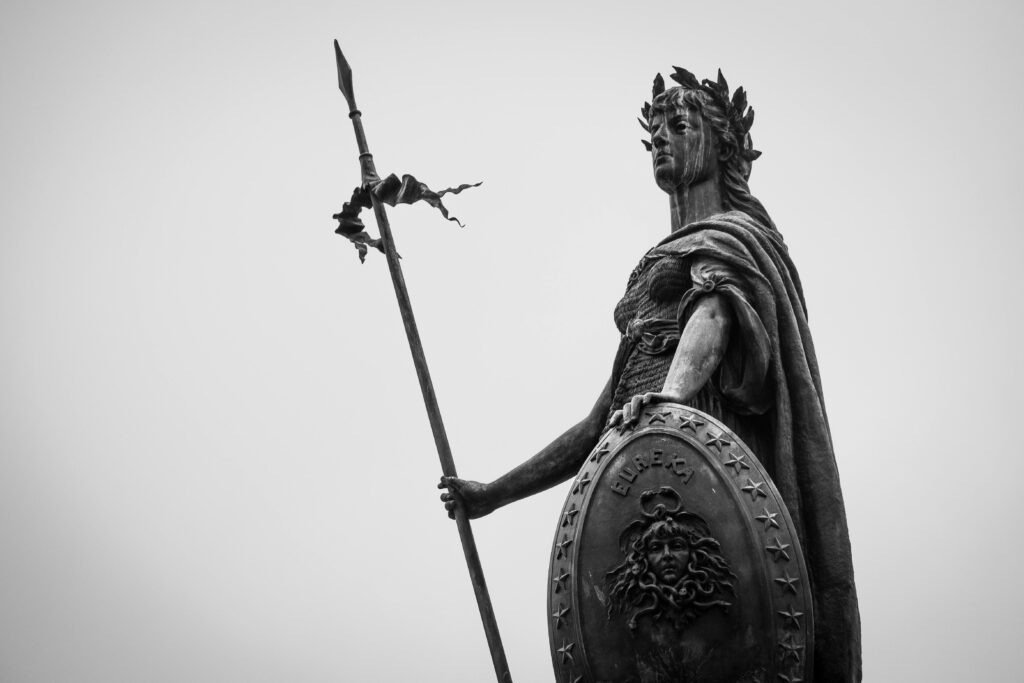 A monochrome photograph showcasing a classic statue holding a spear and shield, exuding timeless strength.